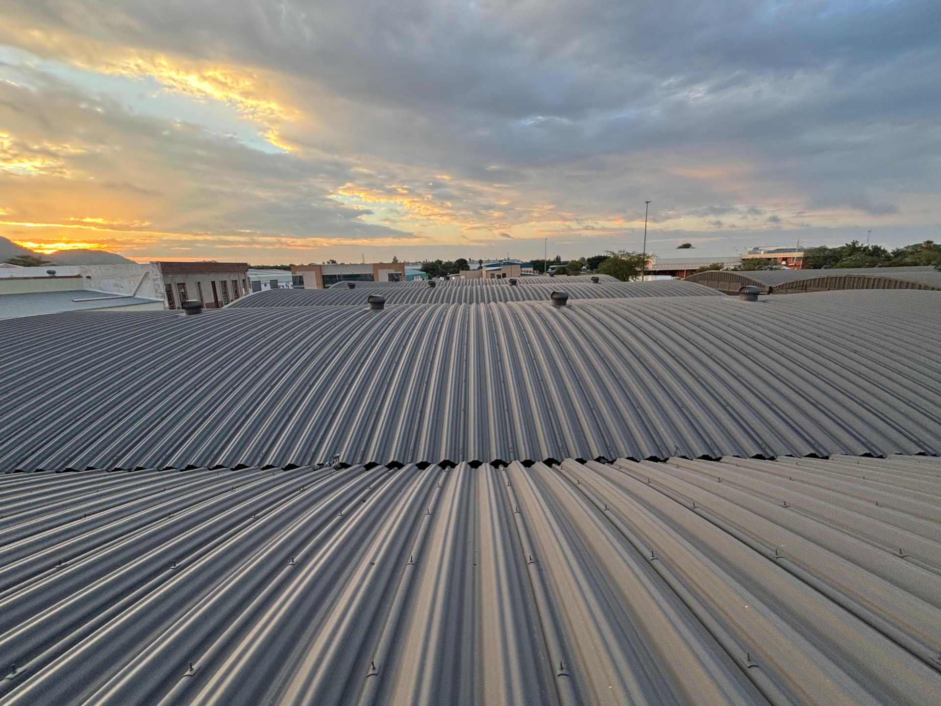 Whirlybird roof ventilators installed along the ridges of a corrugated metal roof at sunset